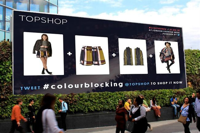 A promotional banner for TopShop clothing in public, with people that are walking by looking at the advertisement