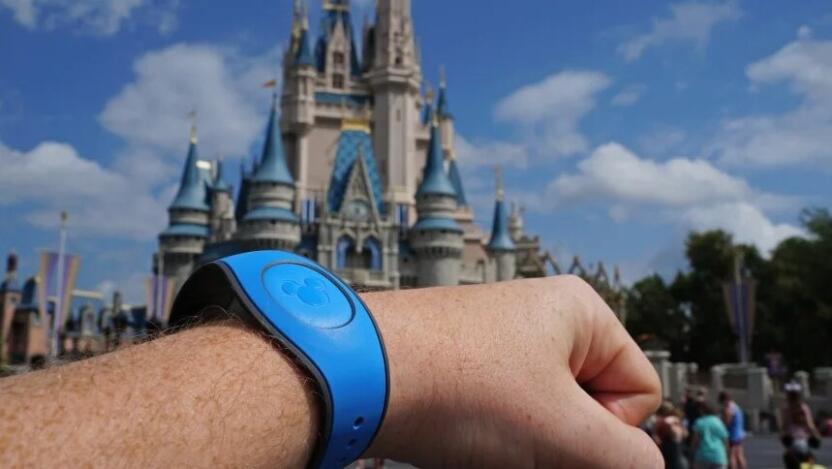 A person holding up a Disney MagicBand on their wrist at a Disney park